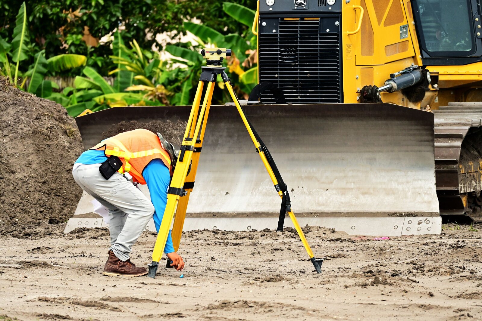 Surveyor setting up a tripod beside a bulldozer on a site.