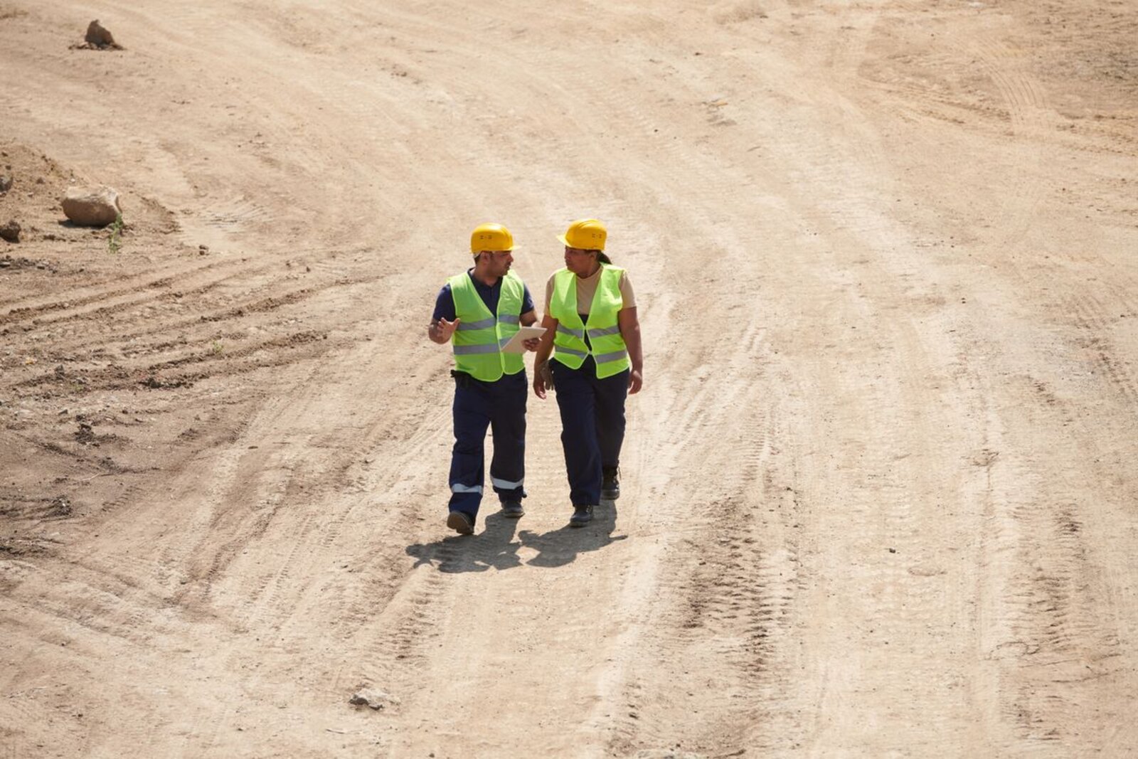 Two workers in safety vests walking across a cleared site.